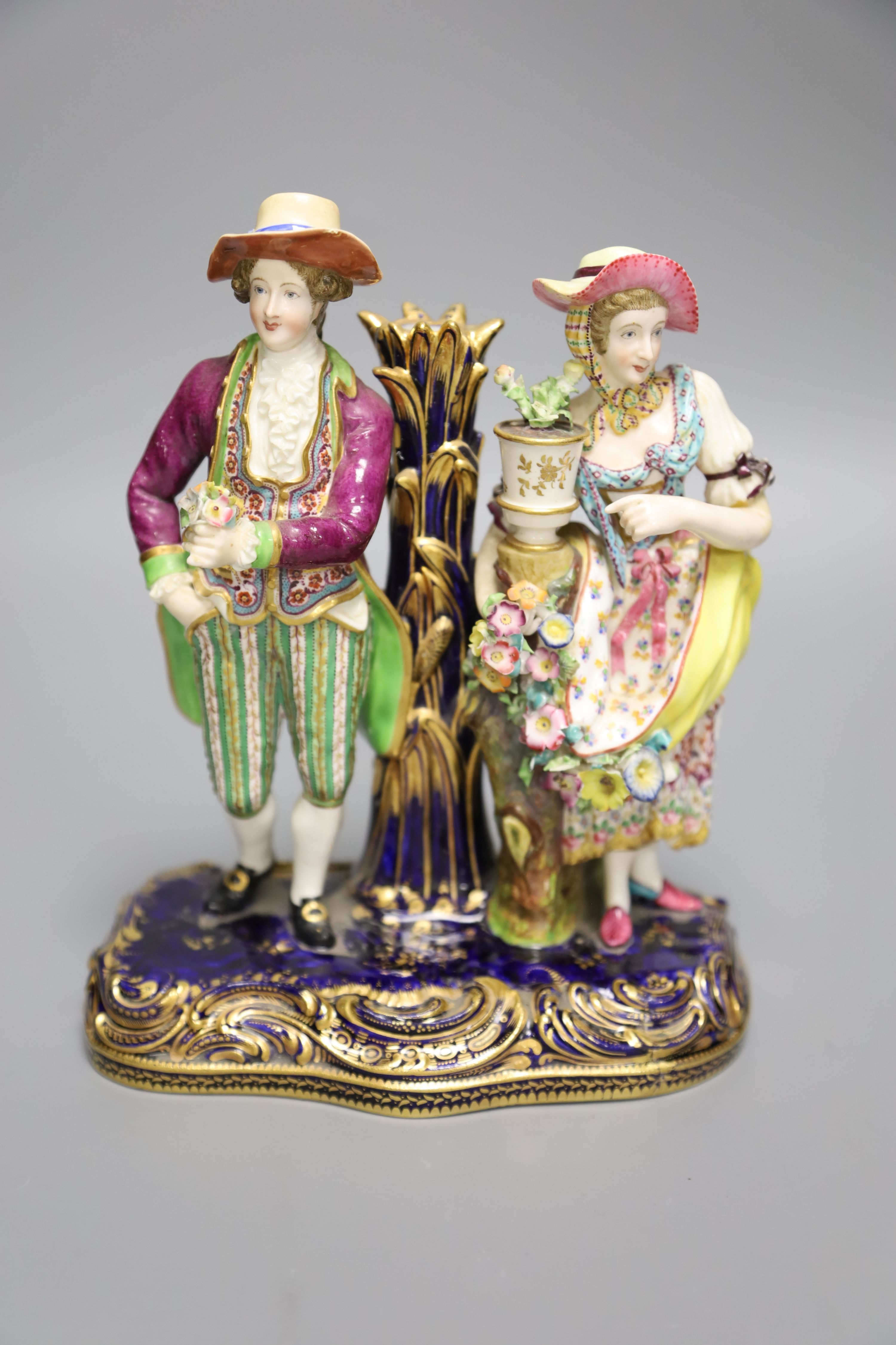 A 19th century Minton figural group and taper stick depicted as a lady and gentleman standing beside a vase of flowers, height 20cm